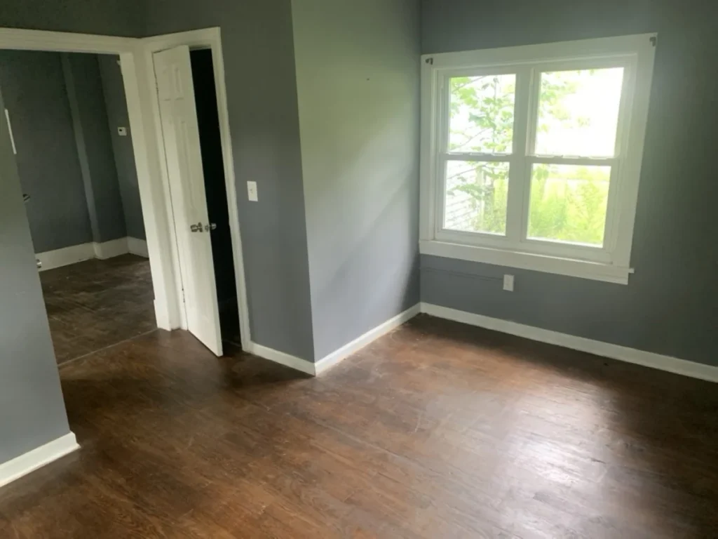 Empty bedroom with gray walls, a window and a dark wood floor after a cleanout
