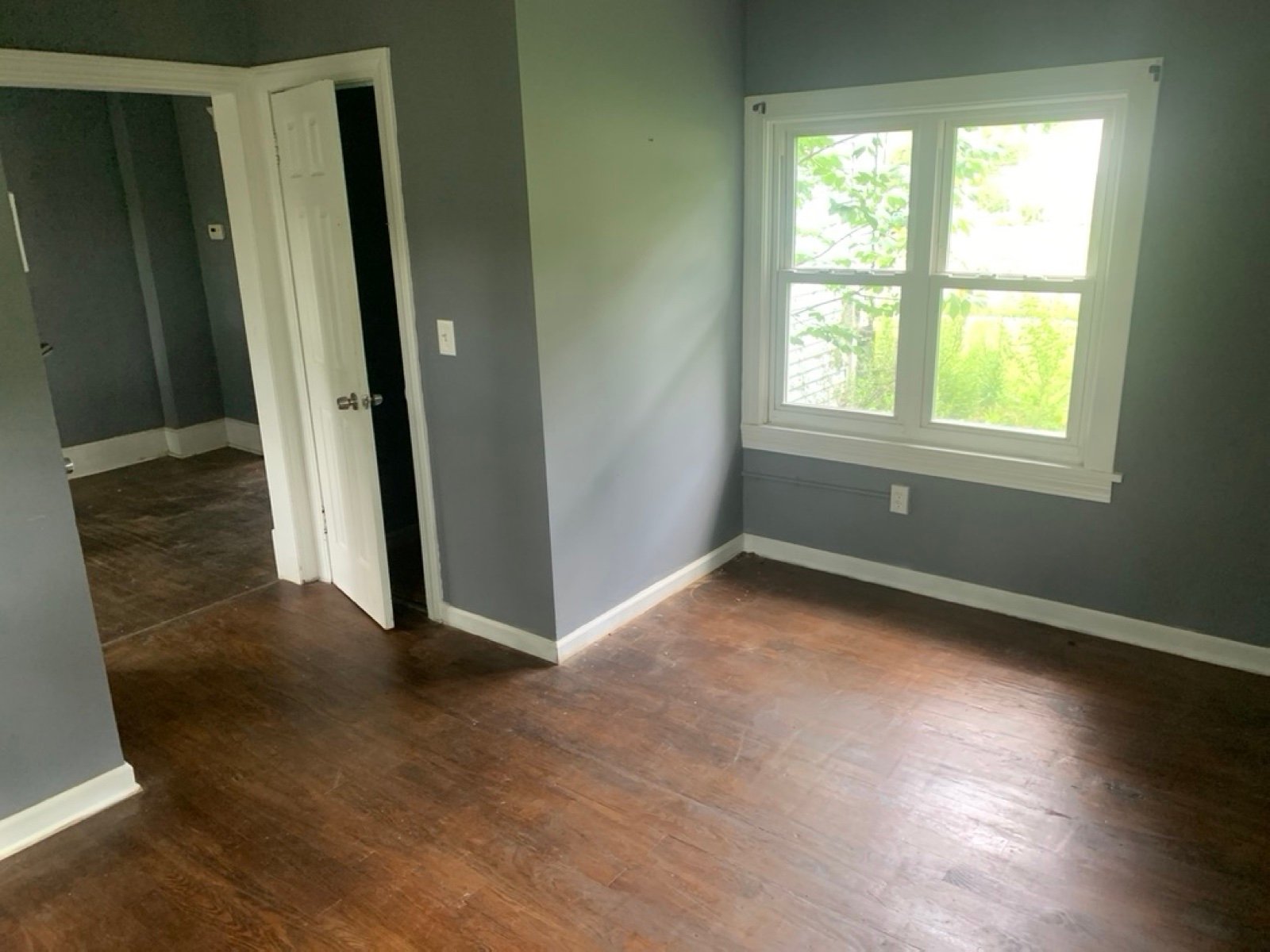 Empty bedroom with gray walls, a window and a dark wood floor after a cleanout