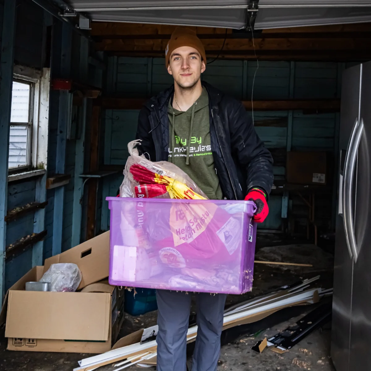 Fly By Junk Haulers crew member carrying a plastic bin out of a garage