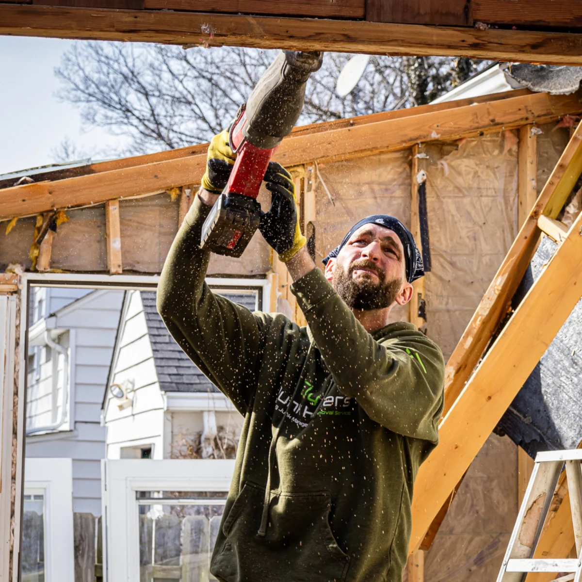 Fly By Junk Haulers crew member cutting wood framing with a reciprocating saw during a demolition