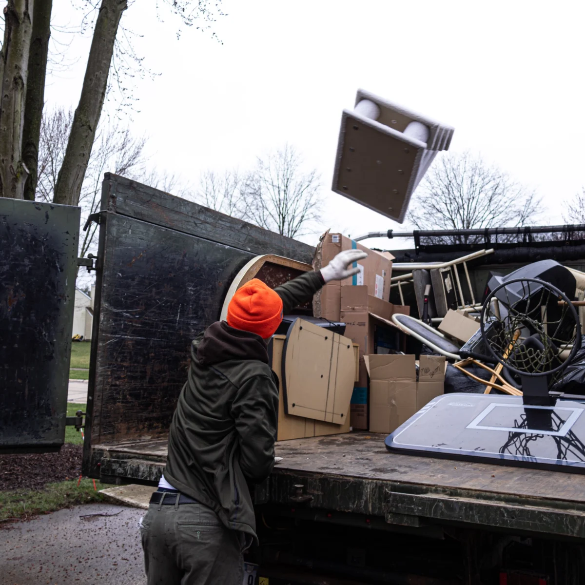 Fly By Junk Haulers crew member in an orange hat tossing furniture into a loaded truck bed