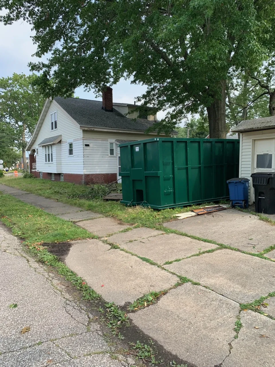 What Can You Put in a Dumpster? (And What Can't Go In) 2 Green dumpster in the driveway beside a white house