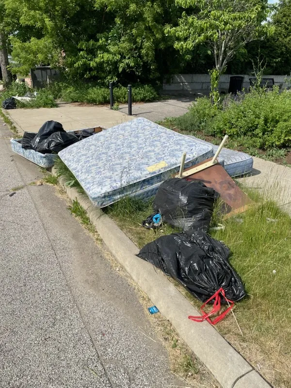 How to Get Rid of a Mattress in Cleveland 2 Mattress and box spring set out on the grass beside a street with black trash bags