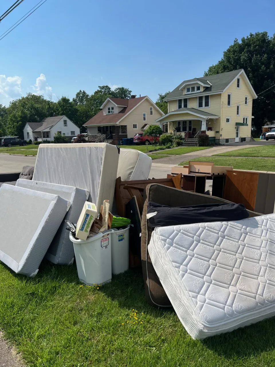 Pile of old mattresses, box springs and furniture set out on a lawn in front of houses for pickup