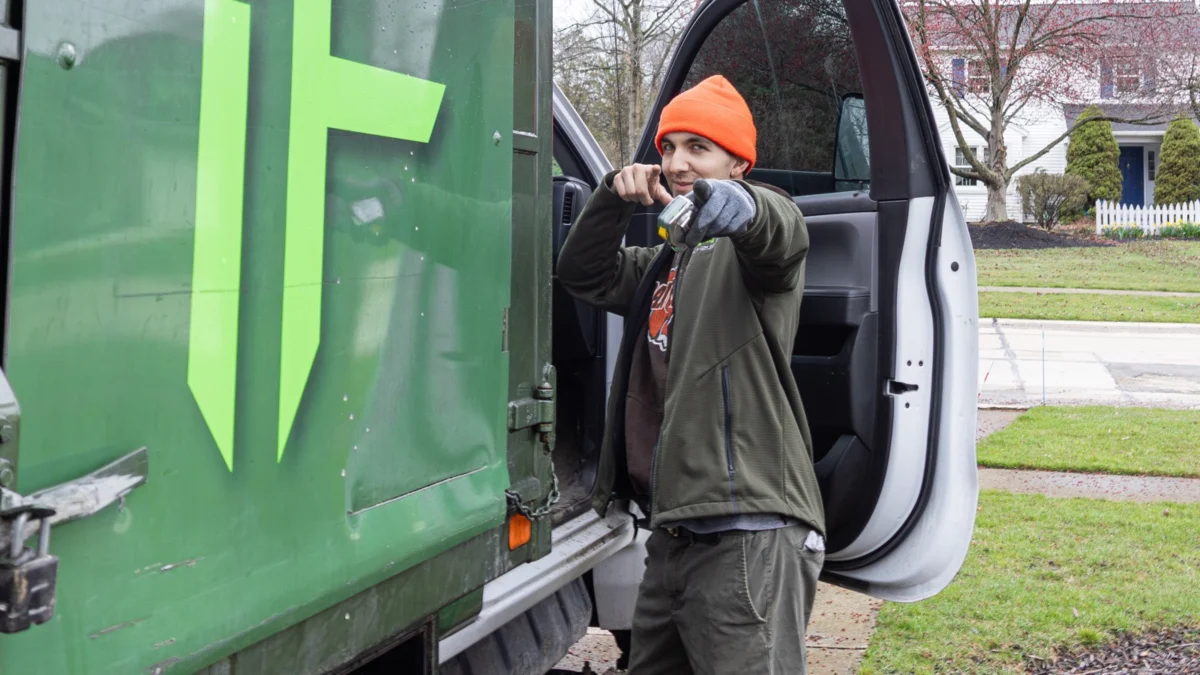 Fly By Junk Haulers truck logo and a crew member by the open cab on a quiet residential street