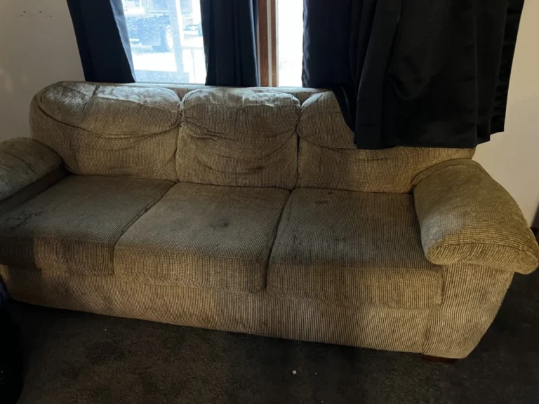 A worn three-cushion fabric couch in front of a window in a living room