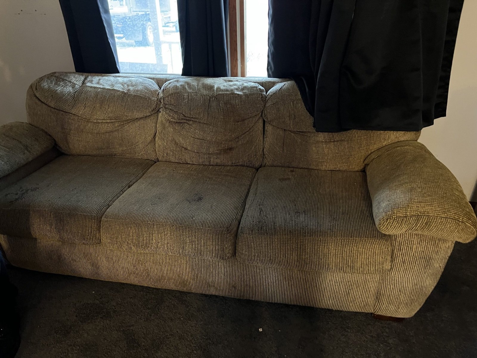 A worn three-cushion fabric couch in front of a window in a living room