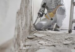 House renovation concept. Construction worker with protective gloves at work breaks the wall with the jackhammer, plaster rubble and ladder on the white background.
