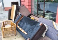 A pile of discarded furniture including a sofa, chair, and various cushions on a city sidewalk, highlighting urban waste and the need for proper disposal or recycling. Vertical picture